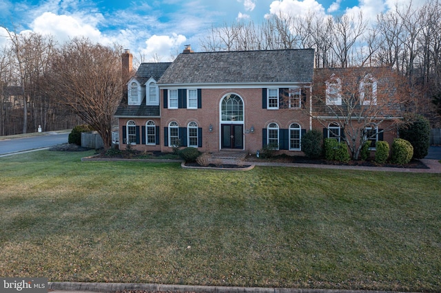 view of front of house featuring brick siding, a chimney, and a front yard