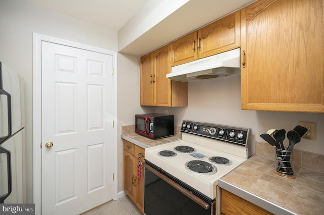 kitchen featuring fridge, tile countertops, light tile patterned floors, and electric range