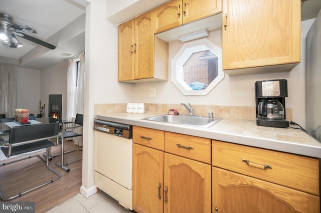 kitchen featuring sink, light tile patterned floors, dishwasher, ceiling fan, and tile counters