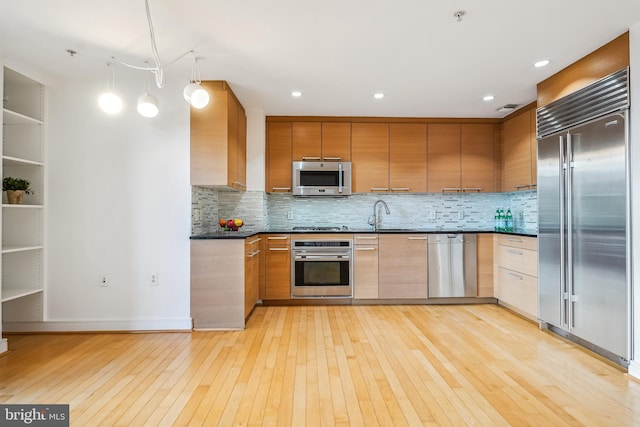 kitchen featuring appliances with stainless steel finishes, light hardwood / wood-style flooring, backsplash, and decorative light fixtures