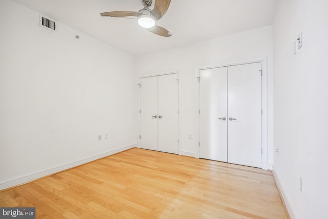 unfurnished bedroom with multiple closets, ceiling fan, and light hardwood / wood-style flooring