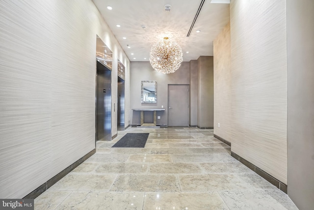 corridor featuring elevator, a towering ceiling, and a notable chandelier