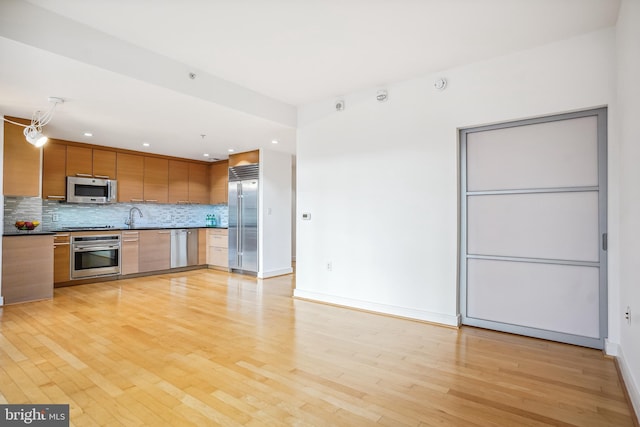 kitchen with stainless steel appliances, sink, light hardwood / wood-style floors, and decorative backsplash