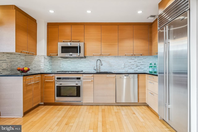 kitchen featuring dark stone countertops, appliances with stainless steel finishes, sink, and light wood-type flooring