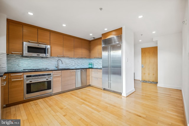 kitchen featuring sink, decorative backsplash, light wood-type flooring, and appliances with stainless steel finishes