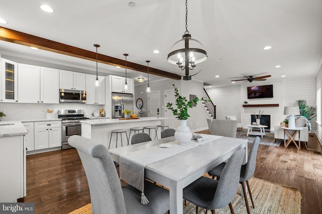 dining area featuring dark wood-type flooring, a large fireplace, beam ceiling, and ceiling fan