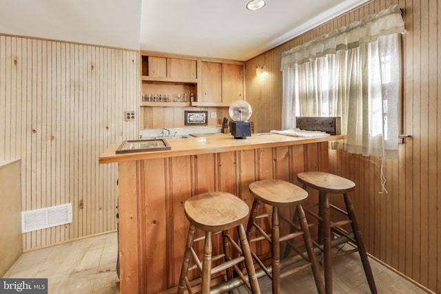 bar featuring sink, light brown cabinets, and wood walls