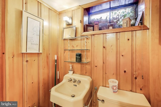 bathroom with toilet, sink, and wood walls