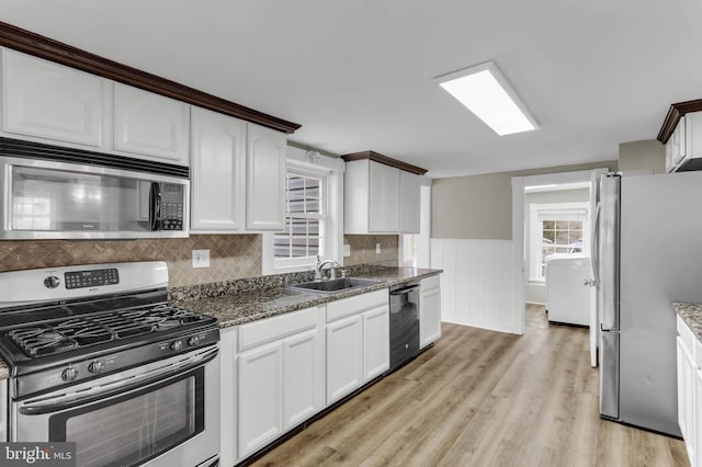 kitchen featuring sink, light hardwood / wood-style flooring, appliances with stainless steel finishes, dark stone counters, and white cabinets