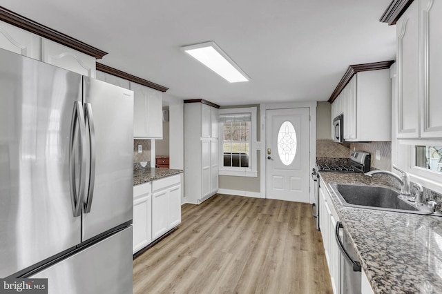 kitchen with sink, appliances with stainless steel finishes, backsplash, white cabinets, and dark stone counters