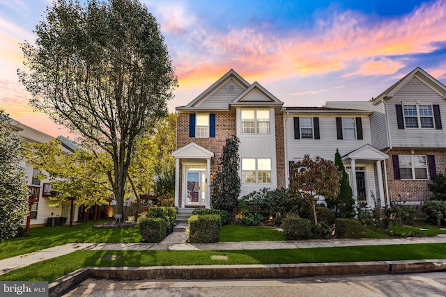 multi unit property featuring cooling unit, brick siding, and a lawn