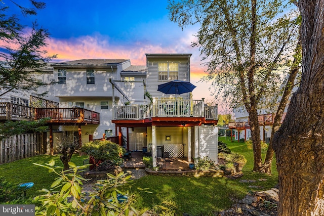 back house at dusk featuring a wooden deck and a yard