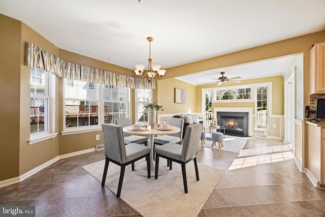 dining area featuring a glass covered fireplace, ceiling fan with notable chandelier, and baseboards