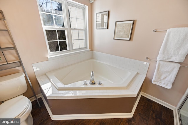 bathroom with a garden tub, toilet, and wood finished floors