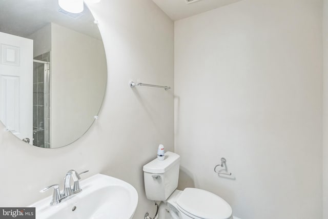 bathroom featuring toilet, a shower with shower door, and sink