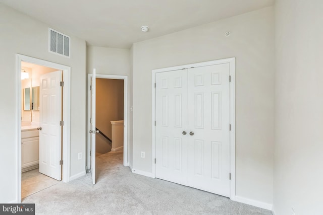 unfurnished bedroom with light colored carpet, ensuite bath, and a closet