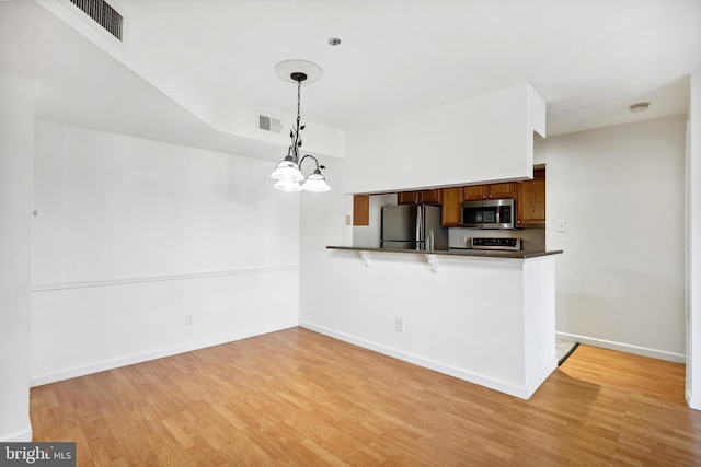 kitchen with appliances with stainless steel finishes, kitchen peninsula, light hardwood / wood-style floors, and hanging light fixtures