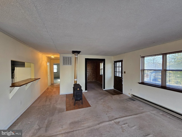 spare room featuring baseboard heating, carpet floors, a textured ceiling, and a wood stove