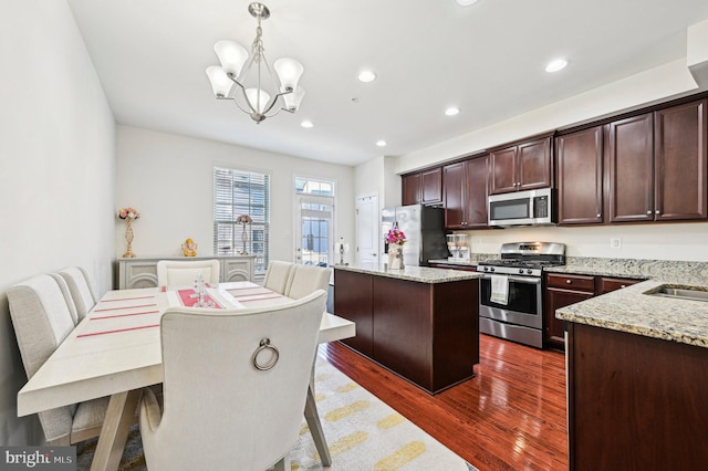 kitchen featuring appliances with stainless steel finishes, a center island, light stone counters, and decorative light fixtures