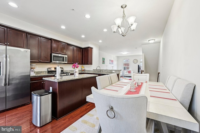 kitchen with decorative light fixtures, a center island, kitchen peninsula, stainless steel appliances, and dark wood-type flooring