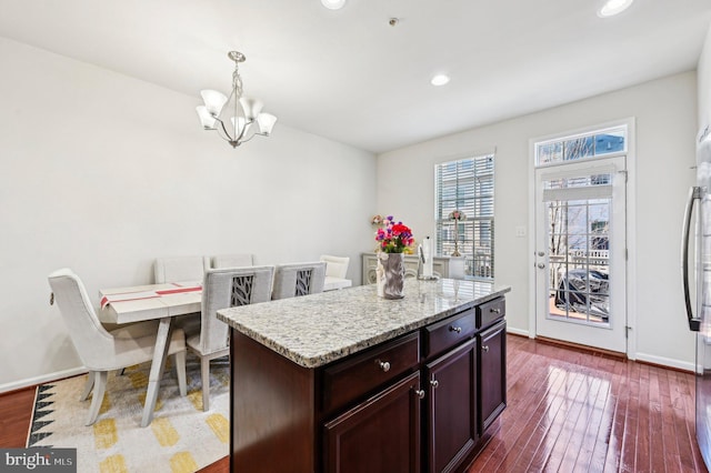 kitchen with an inviting chandelier, dark hardwood / wood-style floors, a kitchen island with sink, and hanging light fixtures