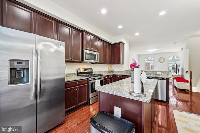 kitchen with a kitchen island, appliances with stainless steel finishes, light stone counters, kitchen peninsula, and dark wood-type flooring