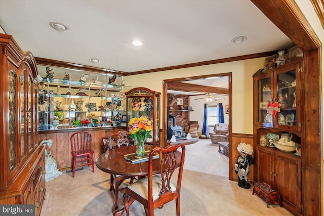 dining space featuring light colored carpet, ornamental molding, and a wood stove