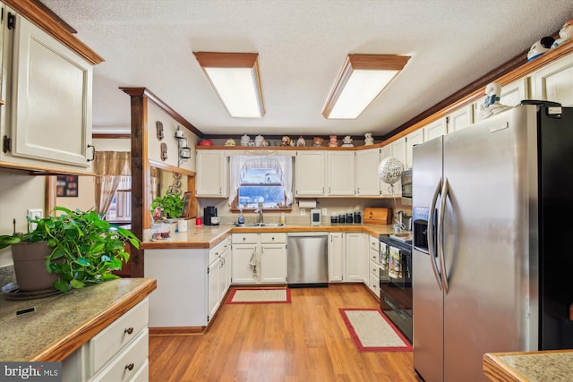 kitchen with light wood-type flooring, stainless steel appliances, sink, and white cabinets