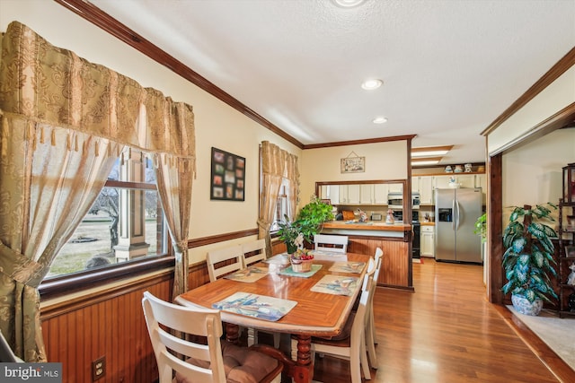 dining area with ornamental molding, wooden walls, light hardwood / wood-style floors, and a textured ceiling