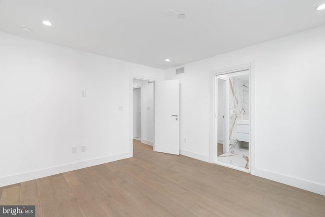 unfurnished bedroom featuring ensuite bathroom and light hardwood / wood-style flooring