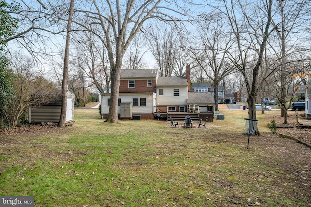 back of house featuring a storage shed, a fire pit, a chimney, a yard, and an outdoor structure