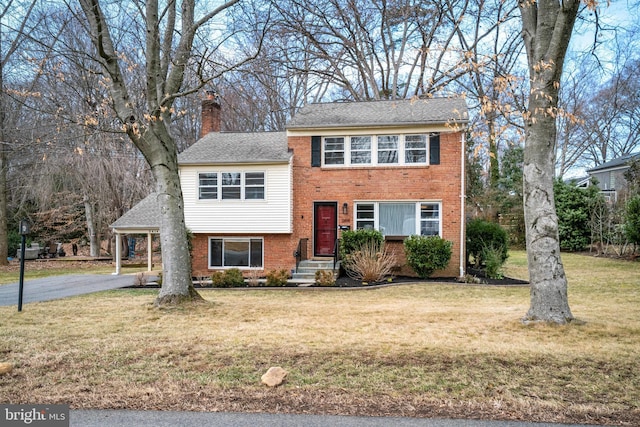 split level home with aphalt driveway, a front yard, brick siding, and a chimney