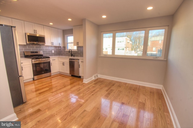 kitchen featuring white cabinetry, sink, backsplash, stainless steel appliances, and light wood-type flooring