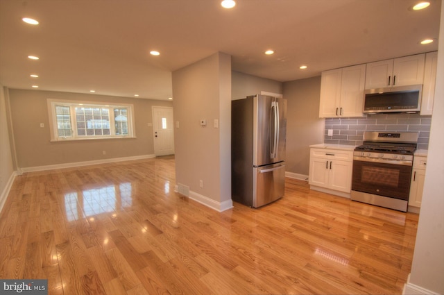 kitchen with appliances with stainless steel finishes, white cabinets, light hardwood / wood-style floors, and decorative backsplash