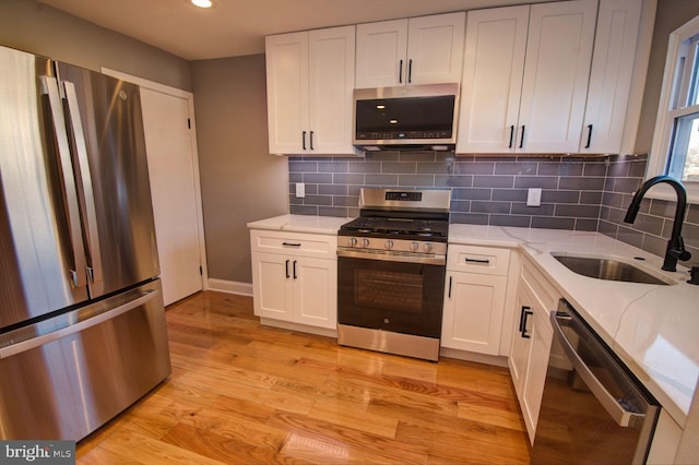 kitchen featuring white cabinetry, stainless steel appliances, sink, and light stone counters