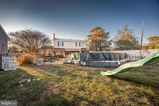 rear view of property featuring a covered pool, a patio area, and a lawn