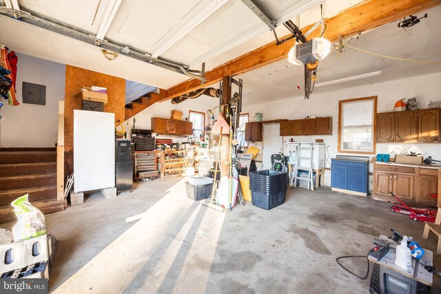 garage featuring a garage door opener, black refrigerator, electric panel, and a workshop area