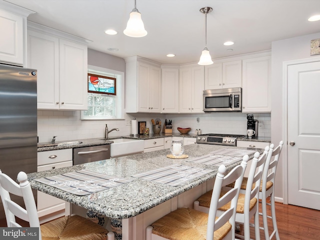 kitchen featuring white cabinets, a kitchen breakfast bar, hanging light fixtures, light stone counters, and stainless steel appliances