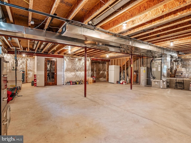 basement featuring water heater, white fridge, and heating unit