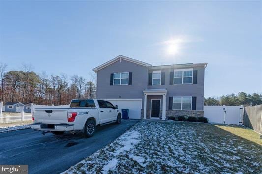 traditional-style house with a garage, aphalt driveway, fence, stone siding, and a gate