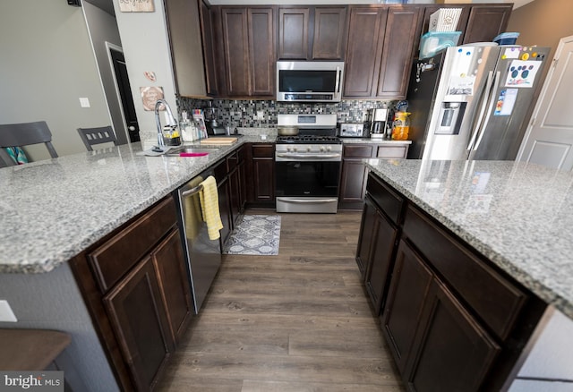 kitchen with dark wood-type flooring, sink, a breakfast bar area, light stone counters, and stainless steel appliances