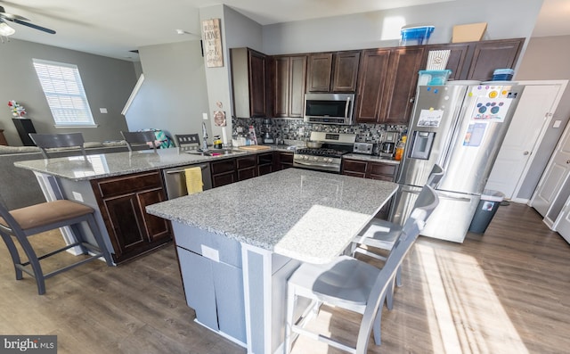 kitchen with sink, a kitchen bar, a center island, light stone counters, and stainless steel appliances