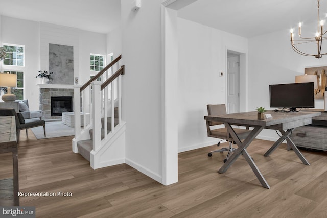 office with hardwood / wood-style floors, a notable chandelier, and a stone fireplace