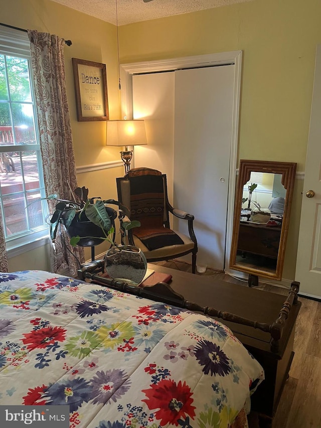 bedroom with a textured ceiling, wood finished floors, and a closet