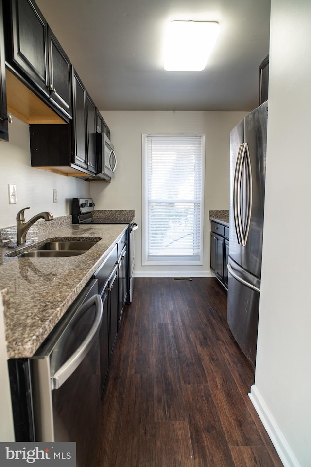 kitchen with appliances with stainless steel finishes, sink, dark stone countertops, and dark hardwood / wood-style flooring