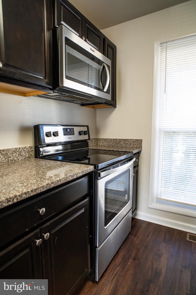 kitchen with dark wood-type flooring, stainless steel appliances, and dark stone countertops