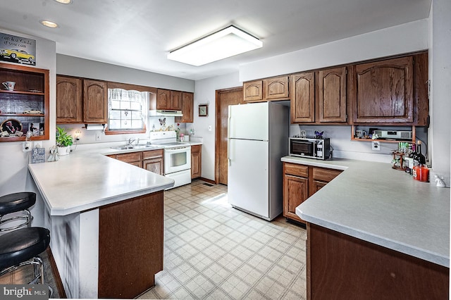 kitchen with white appliances, sink, a kitchen breakfast bar, and kitchen peninsula