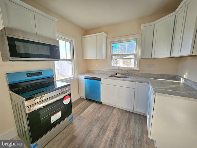 kitchen with appliances with stainless steel finishes, sink, white cabinets, a healthy amount of sunlight, and light wood-type flooring