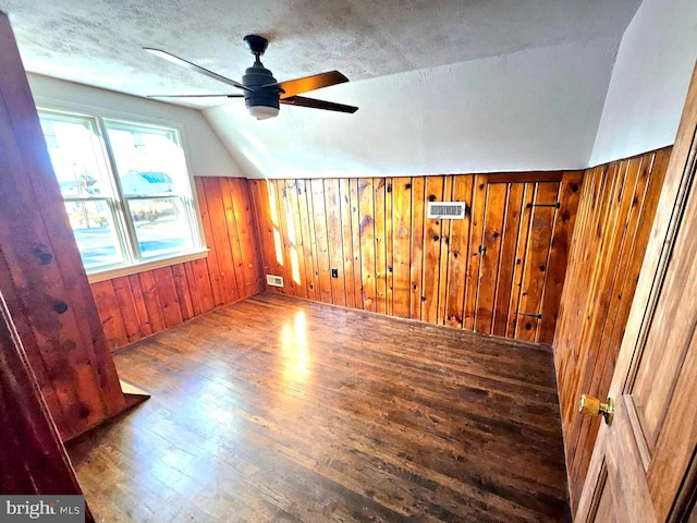 additional living space featuring lofted ceiling, hardwood / wood-style flooring, ceiling fan, wooden walls, and a textured ceiling