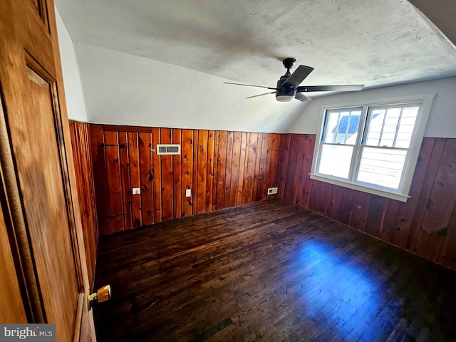 additional living space with ceiling fan, dark hardwood / wood-style flooring, a textured ceiling, and wood walls